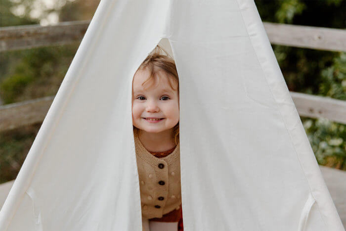 Photo of a young girl with her happy face poking out of a child's teepee